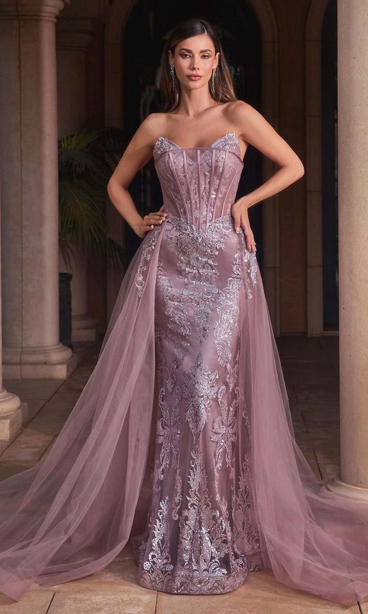 A woman poses gracefully in an elegant setting, wearing the Glitter-Print Strapless Long Prom Dress J858 featuring a mauve hue, silver embroidery, and a sheer tulle overskirt.